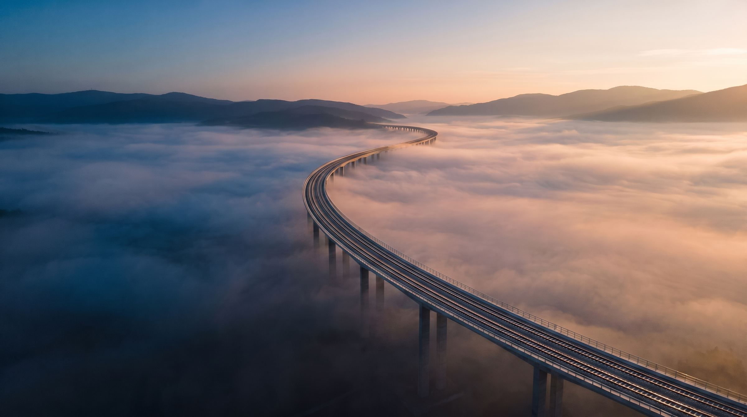 Railway viaduct curving through a valley of low cloud at sunrise